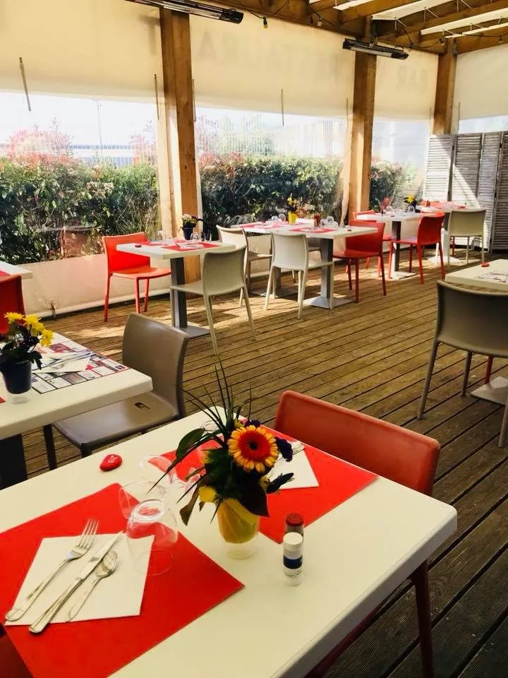 La terraza cubierta del Hangar 27, sillas rojas y caminos de mesa, abierta al jardín